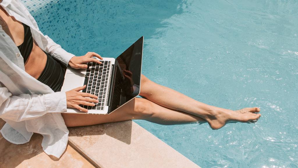 Frau mit Laptop am Pool – recherchiert zur Poolheizung mit Solarenergie