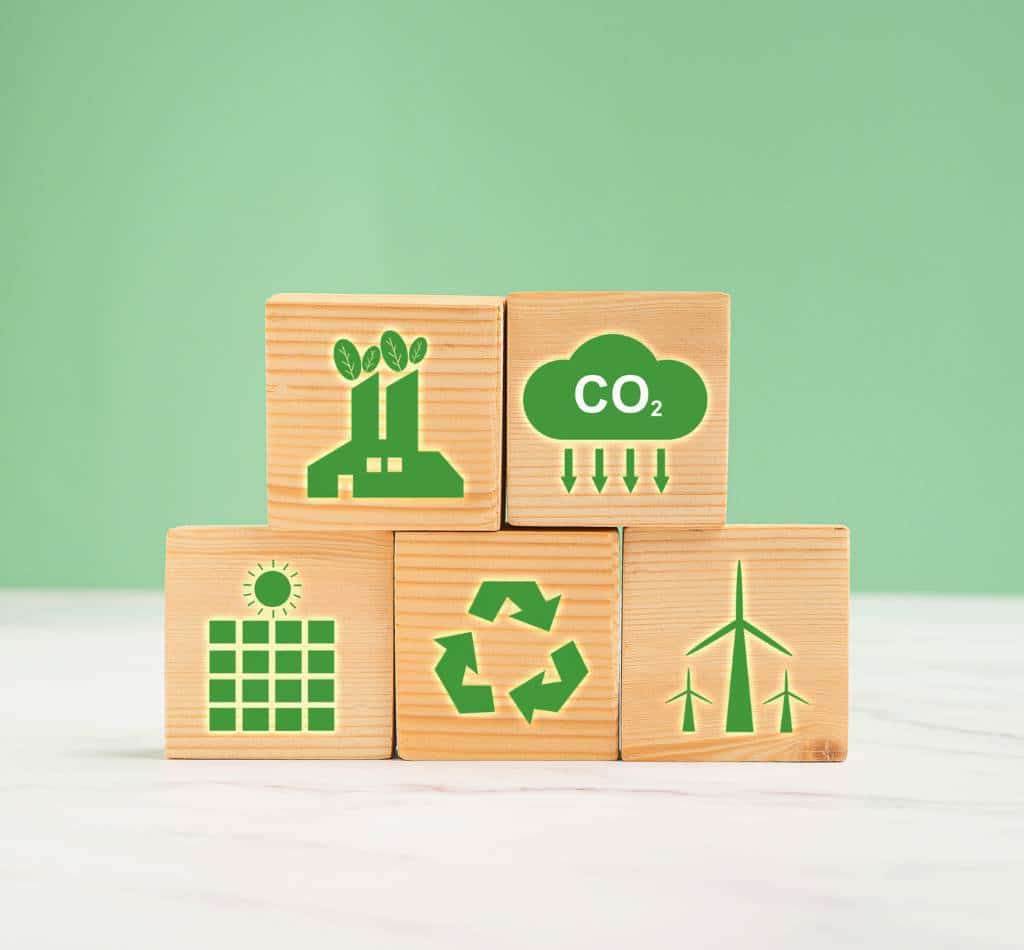 Holzklötze mit Symbolen für CO₂-Reduktion, Photovoltaik, Windkraft und Recycling – Symbolbild für nachhaltiges Energiemanagement in Unternehmen