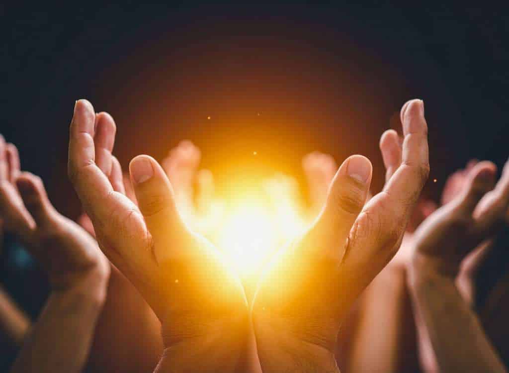 Mehrere Hände, die symbolisch warmes Licht auffangen, stehen für Energie, Wärme und gemeinsames Handeln im Winter.