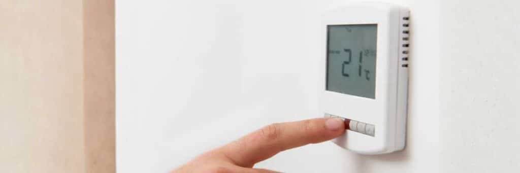 Finger stellt ein digitales Wandthermostat auf 21 Grad Celsius ein.